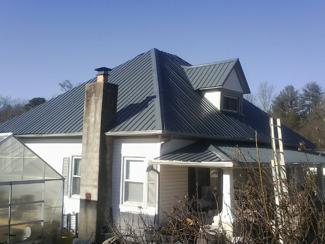 Dark blue standing seam metal roof on a white farmhouse with dormer — Slate & Tile Roof Repair by Roofing Brothers in Volant