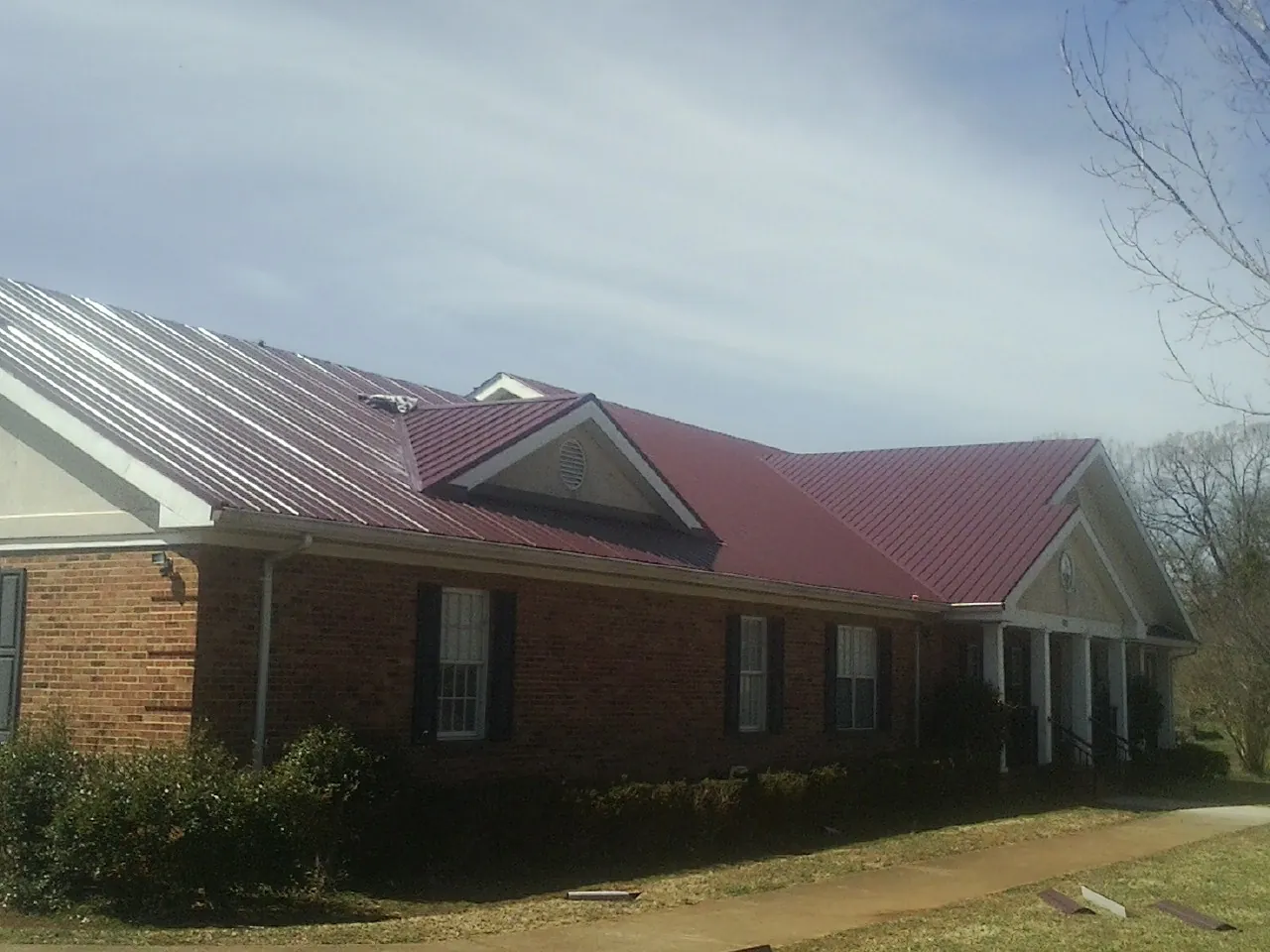 Red metal roof with gabled entries on a long brick building, from a Hail Damage Roof Repair job in Volant