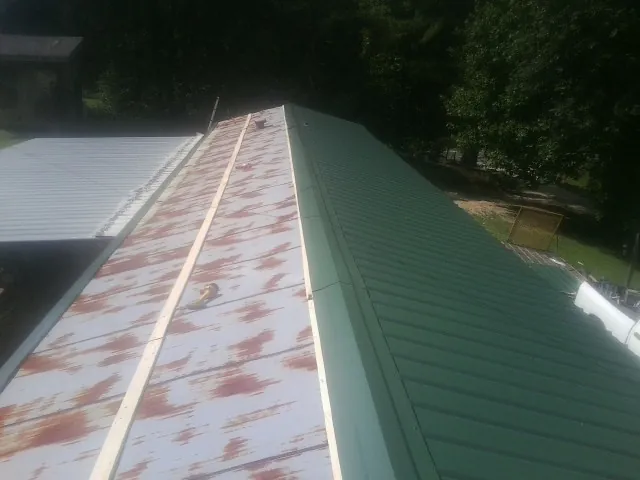 Old rusted panels beside newly installed green metal roofing — Wind Damage Roof Repair by Roofing Brothers in Volant