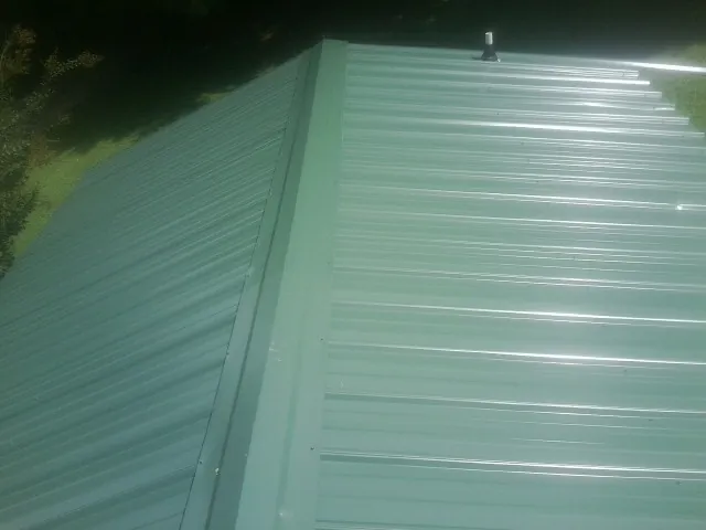 New green metal panels meeting at the ridge of a roof — Flat Roof Repair work by our crew in Volant