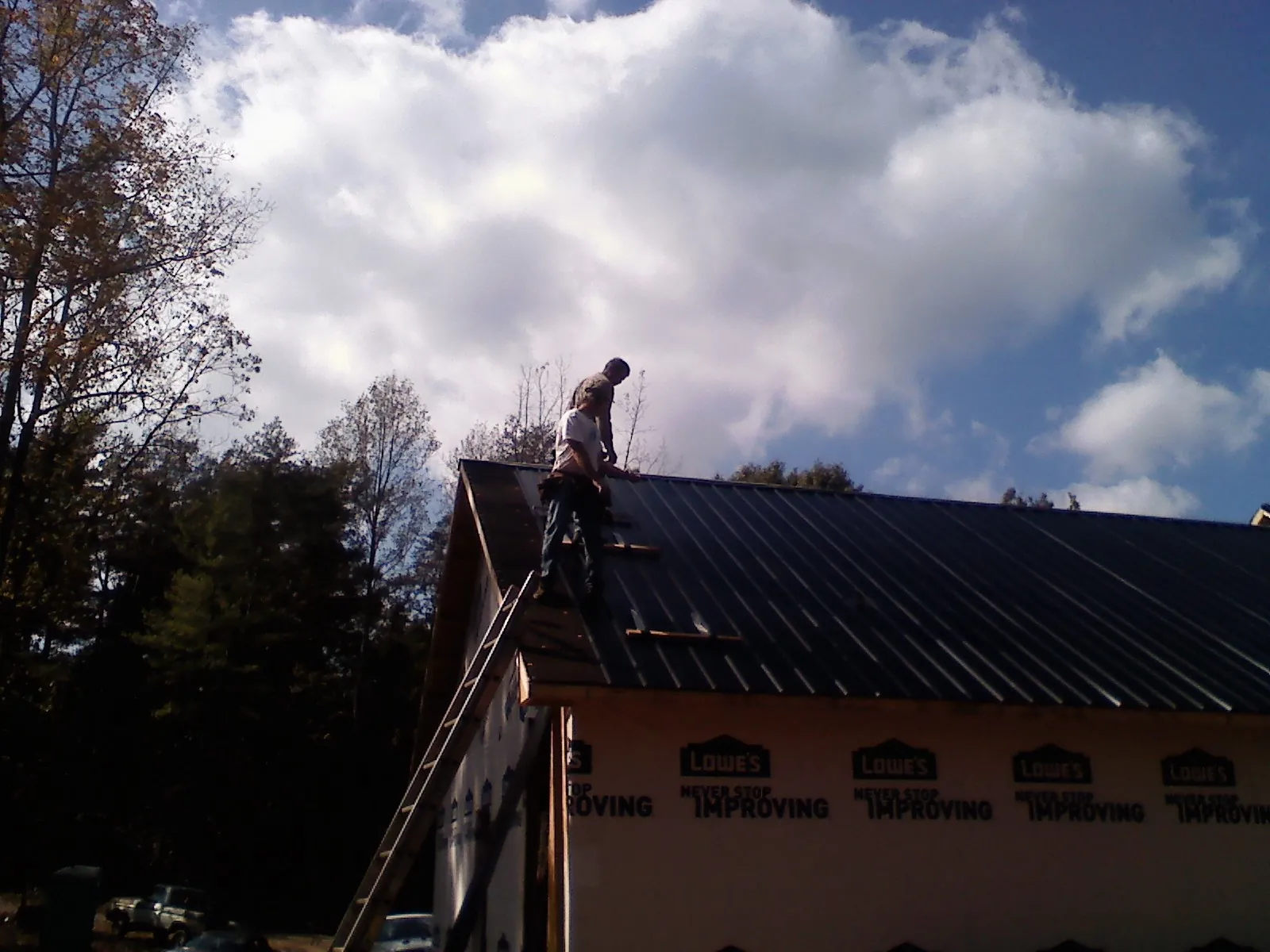 Roofer fastening dark metal panels high against a cloudy sky, from a Roof Inspection job in Volant