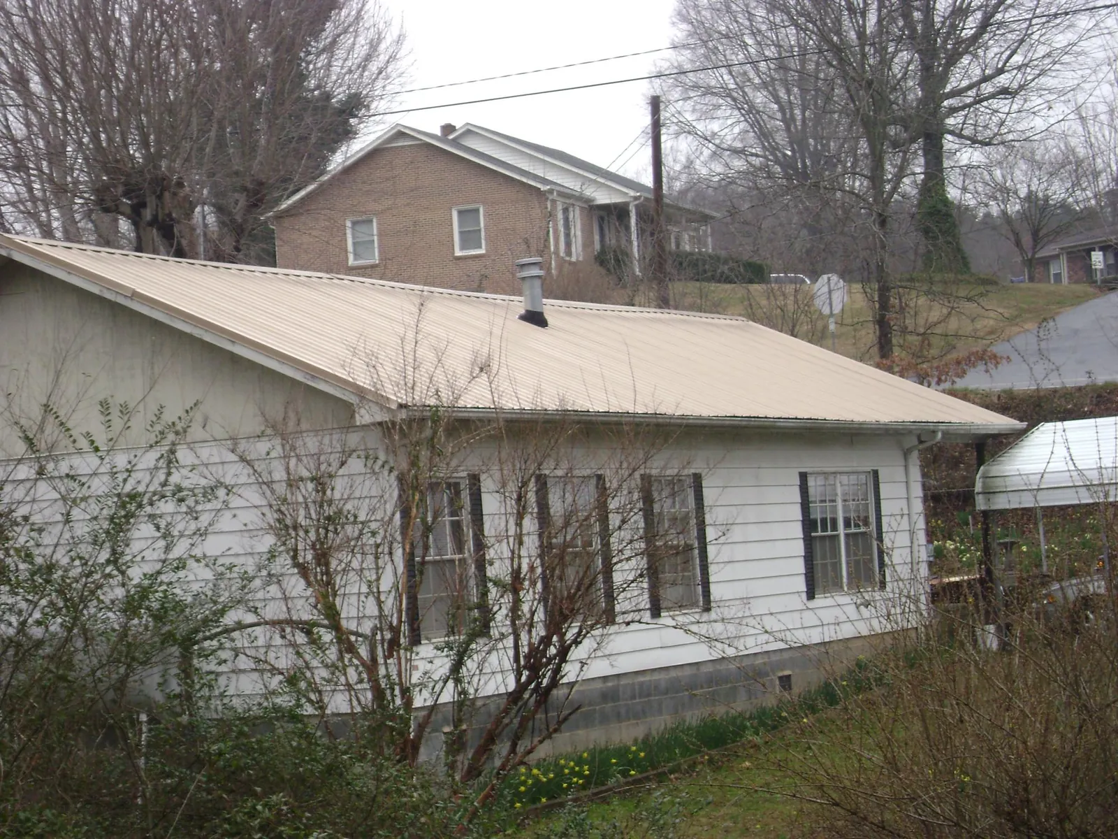 Tan metal roof on a white sided house set into a hillside — Commercial Roofing by Roofing Brothers in Volant